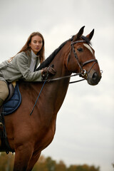 Fototapeta premium Beautiful young woman riding a horse on the field. Sideways to the camera. Freedom, joy, movement