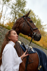 Obraz premium Female horseman going with her brown horse outdoor. Concept of animal care. Rural rest and leisure. Idea of green tourism. Young european woman wearing helmet and uniform