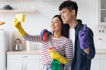 Loving asian couple taking selfie while cleaning kitchen