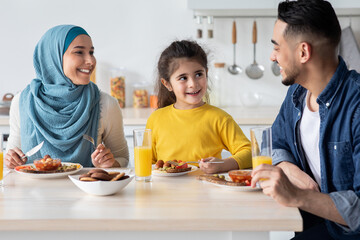 Cheerful Modern Muslim Family With Little Daughter Eating Breakfast Together In Kitchen