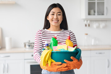 Happy asian woman with cleaning tools standing at kitchen