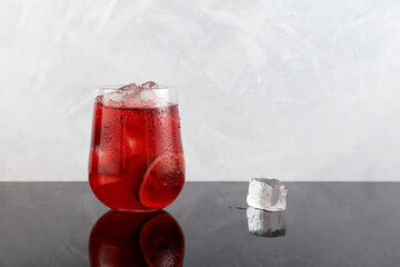 Red refreshing drink with ice or fruit iced tea. Lemonade with hibiscus and passion fruit. Grey background, copy space