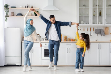 Cheerful arab family of three dancing in kitchen, having fun at home