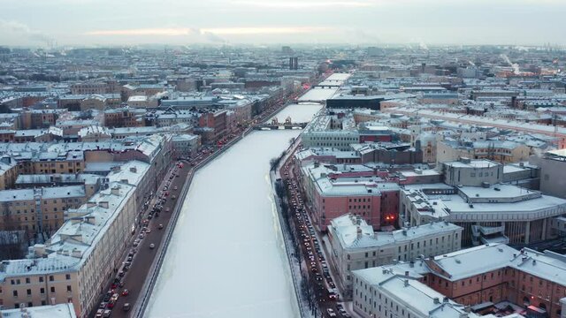 St. Petersburg, Russia, winter 2021: Winter snow covered city center of european ciry, aerial view. Evening illumination, fly over frozen river canal