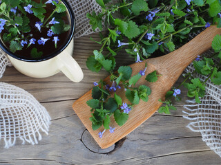 Glechoma hederacea with blue flowers and herbal tea on wooden table, flat layout. Seasonal plant...