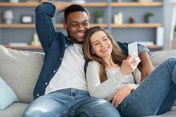 Portrait Of Relaxed Young Multiracial Couple Resting With Smartphone On Couch