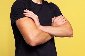 Cropped portrait of young handsome sportive man standing with crossed arms isolated on yellow background. Muscle male body