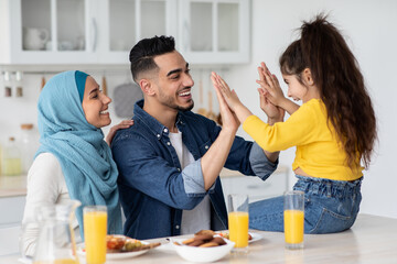 Joyful arabic family of three having fun while eating breakfast in kitchen
