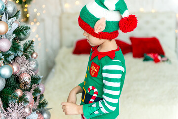 Child decorating Christmas tree at home. Little boy in elf costume and hat with Xmas ornament. Family with kids celebrate winter holidays. Kids decorate living room and fireplace for Christmas.