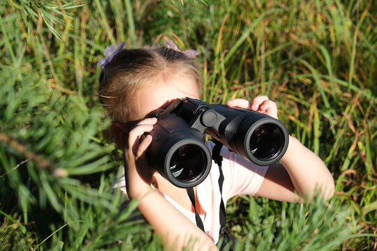 Little girl using binoculars in the forest. Exploring the world. Outdoor activities. Adventure