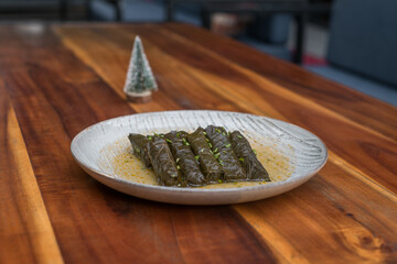 Delicious stuffed grape leaves. Traditional doom Mediterranean cuisine Dolma on white plate with fresh cilantro, on wooden background, close up. 