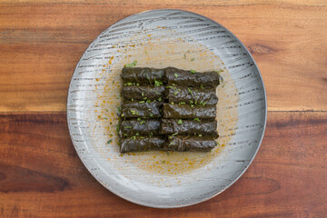 Delicious stuffed grape leaves. Traditional doom Mediterranean cuisine Dolma on white plate with fresh cilantro, on wooden background, close up. 