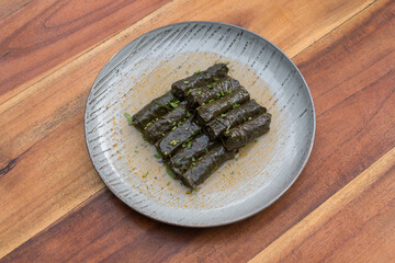 Delicious stuffed grape leaves. Traditional doom Mediterranean cuisine Dolma on white plate with fresh cilantro, on wooden background, close up. 