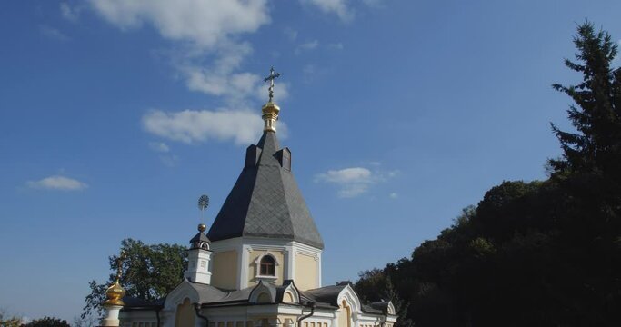 A beautiful view of the Orthodox Christian Church in the monastery, built on a hill covered with conifers on a sunny day, against the backdrop of a cloudless sky.