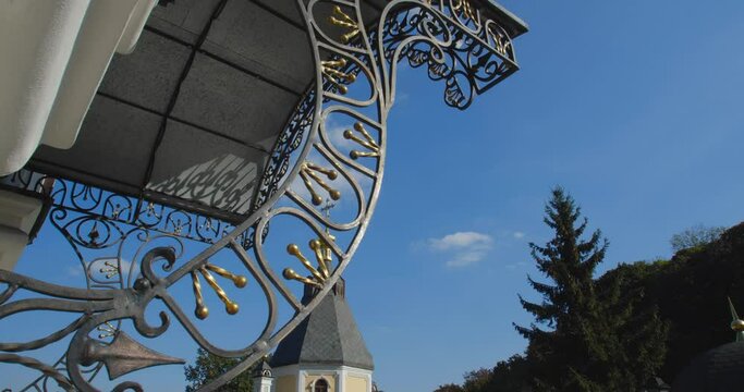 A beautiful view of the Orthodox Christian Church in the monastery, built on a hill covered with conifers on a sunny day, against the backdrop of a cloudless sky.