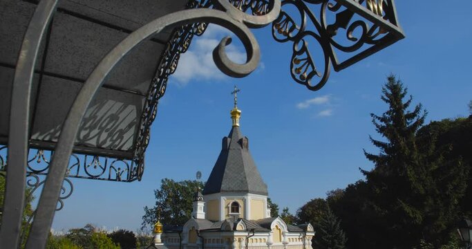 A beautiful view of the Orthodox Christian Church in the monastery, built on a hill covered with conifers on a sunny day, against the backdrop of a cloudless sky.