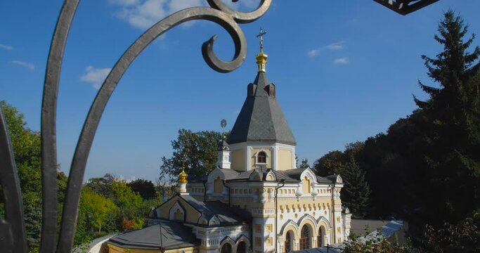 A beautiful view of the Orthodox Christian Church in the monastery, built on a hill covered with conifers on a sunny day, against the backdrop of a cloudless sky.