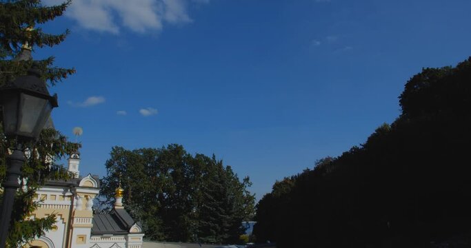 A beautiful view of the Orthodox Christian Church in the monastery, built on a hill covered with conifers on a sunny day, against the backdrop of a cloudless sky.