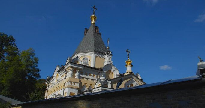 A beautiful view of the Orthodox Christian Church in the monastery, built on a hill covered with conifers on a sunny day, against the backdrop of a cloudless sky.