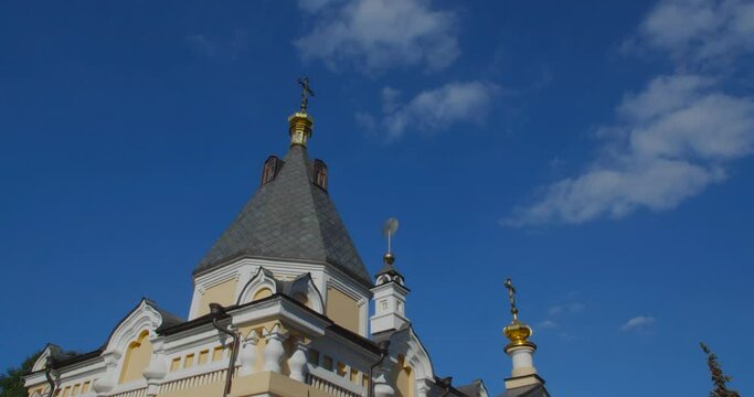 A beautiful view of the Orthodox Christian Church in the monastery, built on a hill covered with conifers on a sunny day, against the backdrop of a cloudless sky.