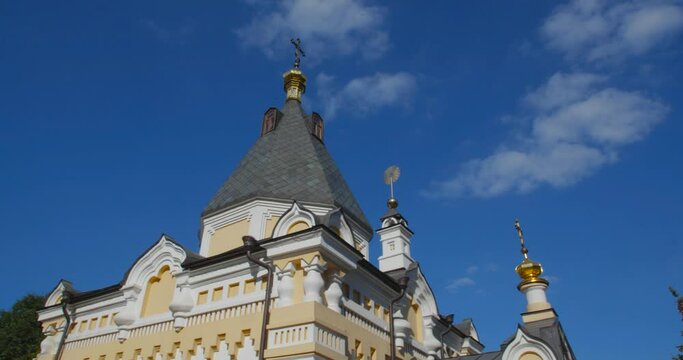 A beautiful view of the Orthodox Christian Church in the monastery, built on a hill covered with conifers on a sunny day, against the backdrop of a cloudless sky.