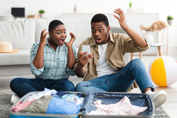 Shocked African Couple With Smartphone Reading Travel News At Home