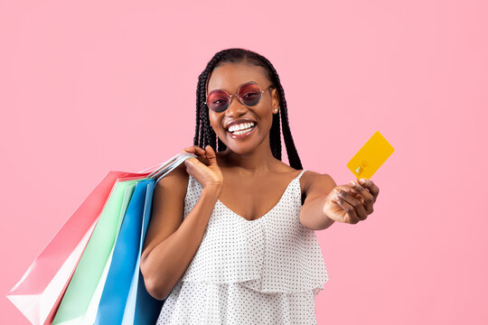 Happy Customer. Joyful Black Lady In Summer Wear Holding Colorful Shopping Bags And Credit Card Over Pink Background