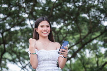A pretty young asian lady pumps her fist in victory after receiving good news on her phone.