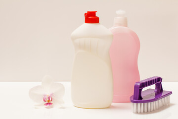 Bottles of dishwashing liquid and brush on white background.
