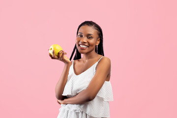 Vitamins for healthy teeth and beautiful skin. Lovely African American woman holding ripe green apple on pink background