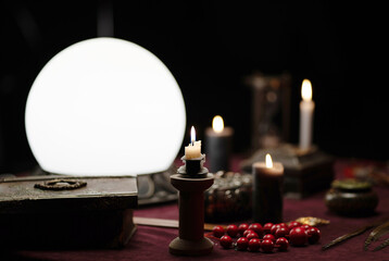 Photo of objects for fortune telling - white crystal ball, candles, book.