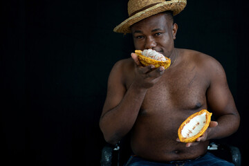 Happy shirtless African man farmers with open cocoa pod and smells it, black background
