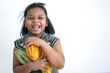Happy little African girl holding cocoa fruit in arm, Cacao fruits which is used as raw material to...