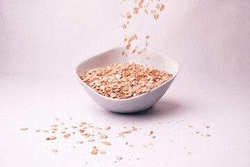Healthy breakfast. Dry rolled oatmeal in bowl isolated on white background. Top view. Oat flakes in...