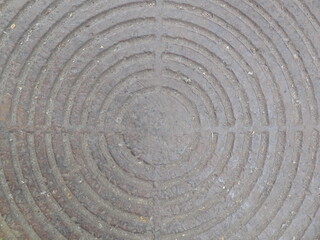 An old rusty cover of the inspection hatch of urban communications (communications, sewerage, drainage, etc.). There is a pattern of concentric circles on the round metal element.