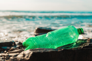 A green plastic bottle is lying on the shore of oken. Close-up. Copy space. The concept of...
