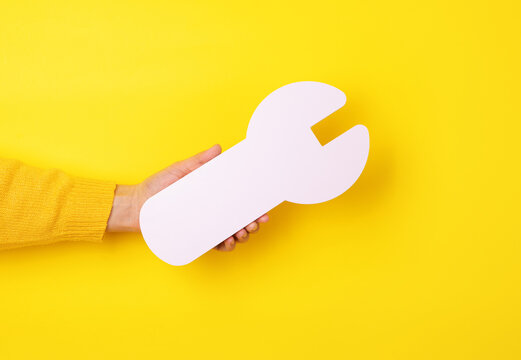 hand holding white wrench, repair symbol in hand over yellow background