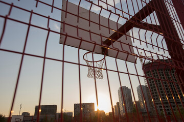 a basketball board with rim and net behind red fence on on buildings background. Tyufeleva Roshcha...