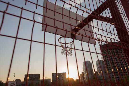 a basketball board with rim and net behind red fence on on buildings background. Tyufeleva Roshcha park, Zilart. !melk landscape architecture urban design