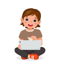 Cute little girl sitting on floor using digital tablet touching screen browsing internet, doing homework, and playing games. Kids and electronic gadget devices concept for children