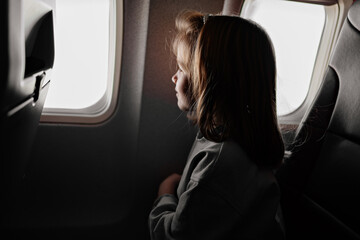 a little girl sits in an airplane seat by the window.