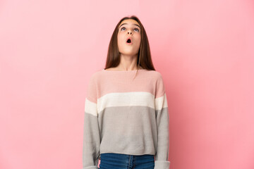 Little girl isolated on pink background looking up and with surprised expression