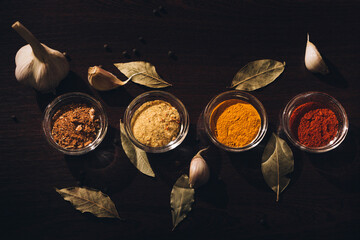 Different spices in glassware on a dark background with garlic, bay leaves and black pepper