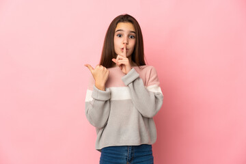 Little girl isolated on pink background pointing to the side and doing silence gesture