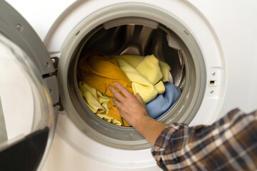 Woman puts bright clothes into a washing machine.