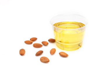 Yellow almond oil in a clear bowl and several almonds on a white background