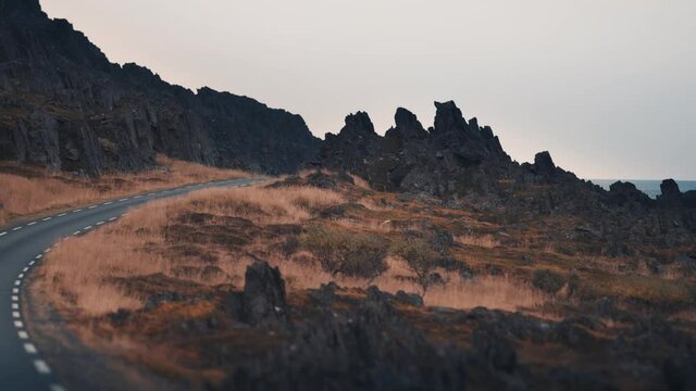 Dashcam view. Driving on the narrow asphalt road through the dark rocky landscape.
