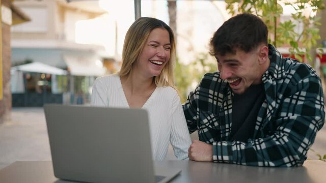 Young couple smiling confident using laptop at coffee shop terrace
