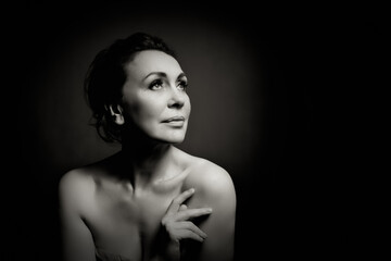 Portrait of a sensual fifty year old woman on grey studio background. Monochrome shot.
