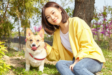 Young woman sitting on the grass in the park and playing with a dog